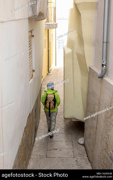 A woman walks through a narrow alley in the resort of Baska, Krk Island, Kvarner Bay, Primorje-Gorski kotar County, Croatia, Europe