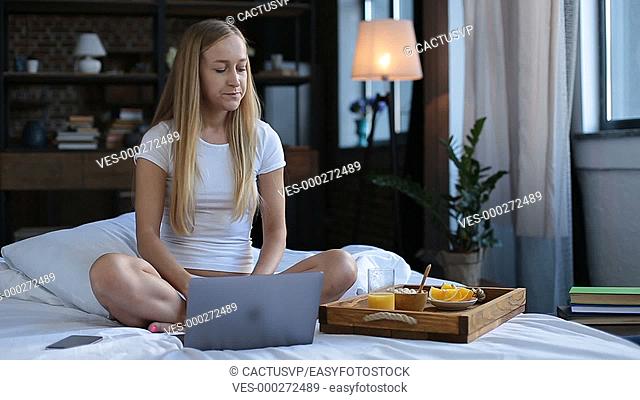 Smiling woman working on laptop in bed