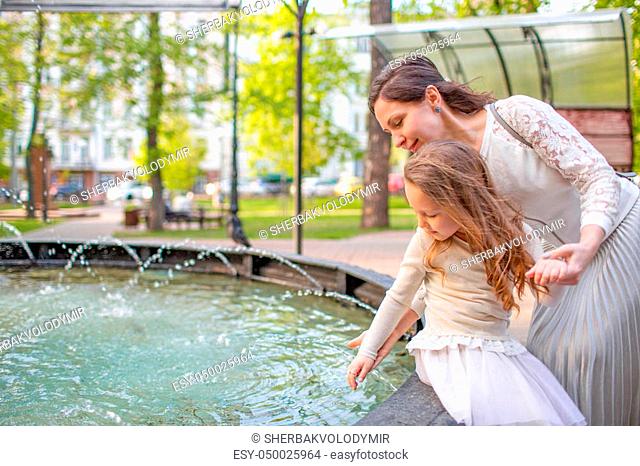 Woman with child playing against splashes of water in the summer. mother and daughter at the fountain in the park