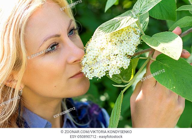 Pretty romantic blonde woman in the city park on a spring sunny day. Spring blossom and green leaves are at the background