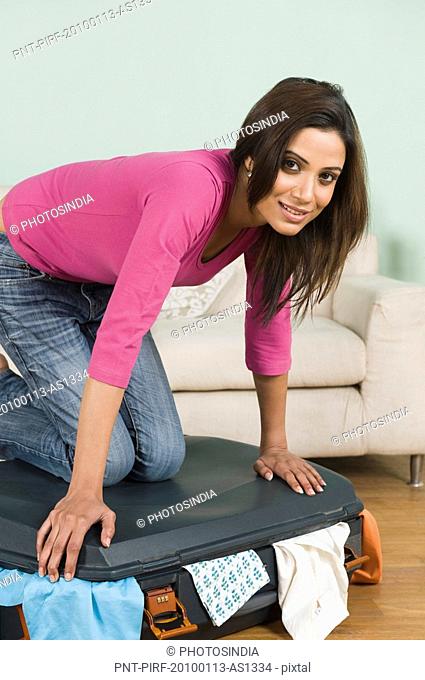 Woman trying to close overfull suitcase