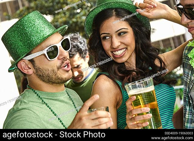 Group of people holding beer glasses dancing and wearing green themed St. Patrick's Day clothing