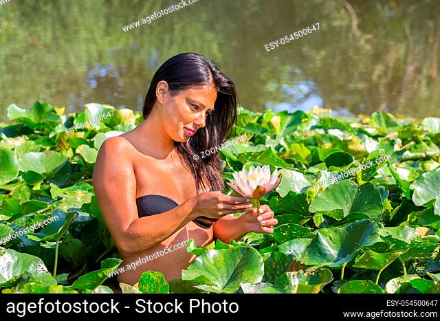 Young colombian woman holding white water lily flower in european pond
