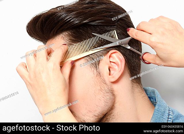 Closeup portrait of handsome young man having haircut in studio. Hairdresser cutting man#39;shair with scissors over white background