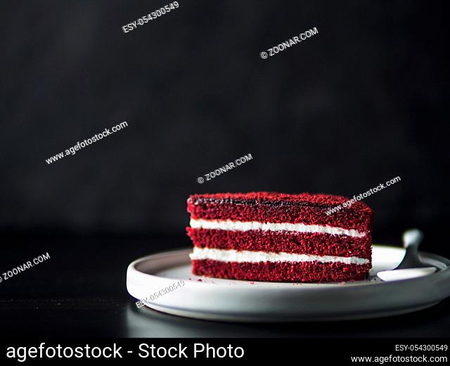 Piece of red velvet cake with perfect texture in matte plate on black tabletop. Slice of delicious homemade red velvet cake with raspberry and chocolate