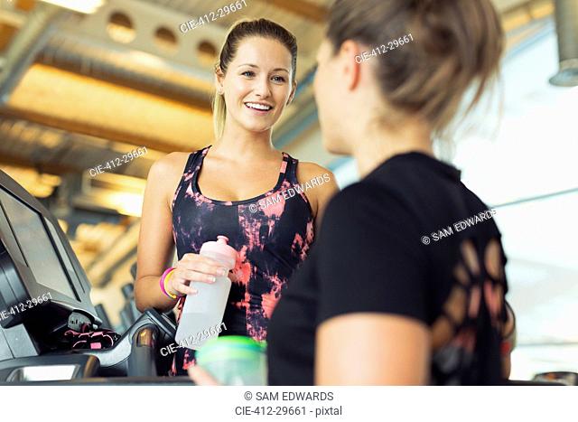 Smiling women talking and drinking water at gym
