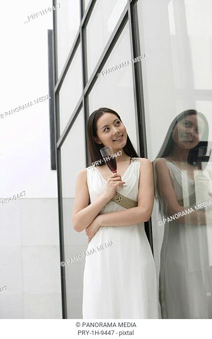 Young woman with wineglass standing by glass wall