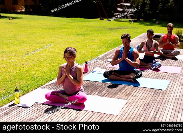 Men and women sitting with hands clasped while meditating on floorboard in public park