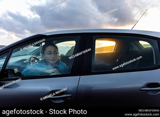 Young woman looking out through car window at sunset