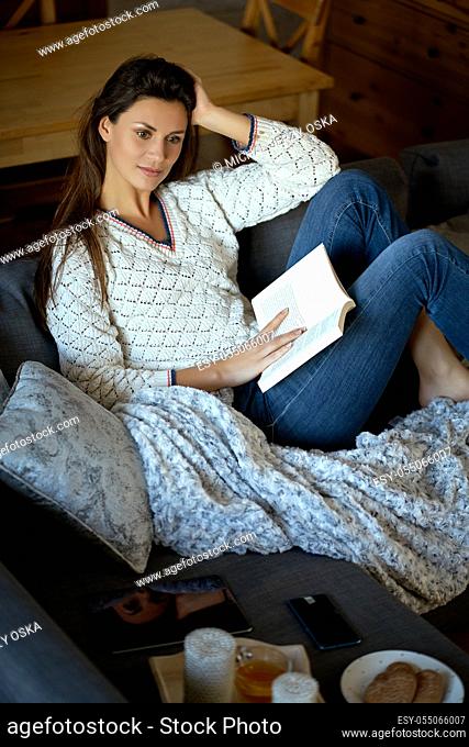 beautiful young brunette woman reading a book on a gray sofa