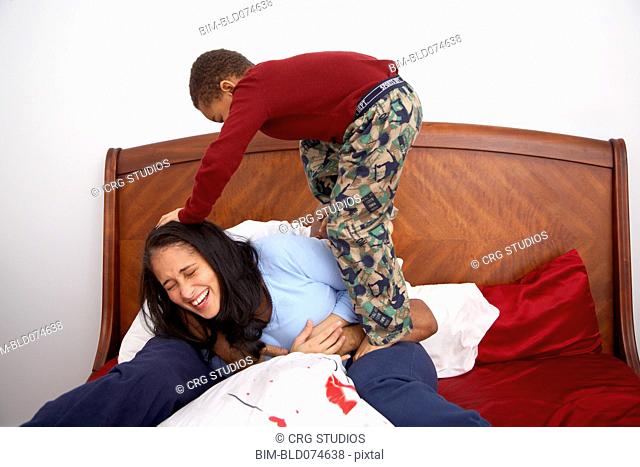 Mixed race boy tackling parents in bed