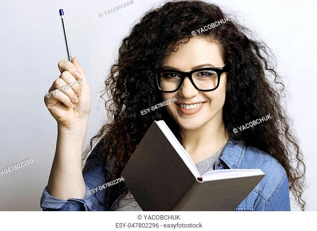 At last eureka. Pleased girl in glasses thinking up an idea, smiling and keeping a pen in her right hand