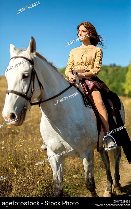 Beautiful girl riding a white horse in a field in profile to the camera