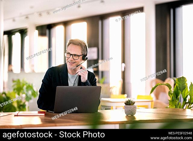 Male customer service representative with laptop looking away while talking through headset at cafeteria