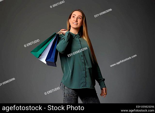 happy blonde woman holding shopping bags with purchases on gray background