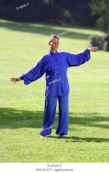 Chan Mi Qi Gong - woman wearing a blue kimono in the nature doing exercise fŸr relaxation - against stress , abnormal attitude , hardening