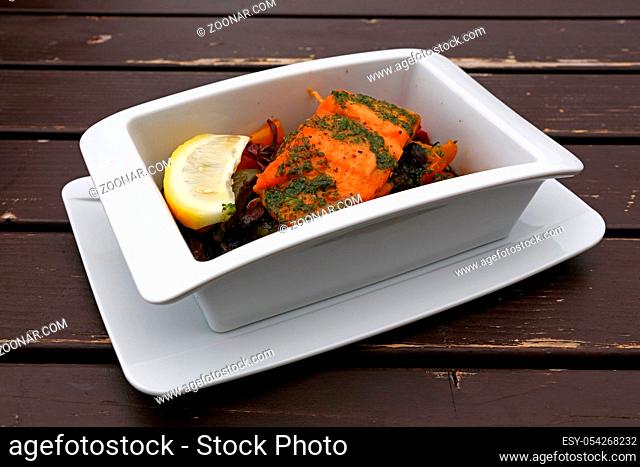 Close up portion of baked or roasted salmon with vegetables in white bowl over table, elevated top view, directly above