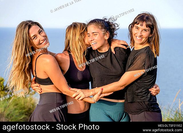 Happy mature female friends with arms around standing together on cliff