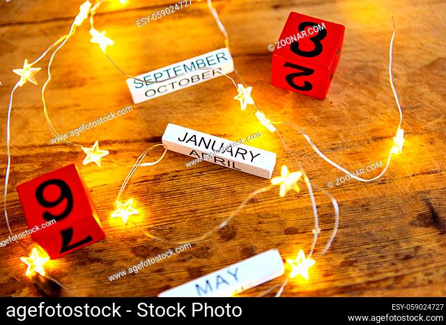 Perpetual calendar on a wooden table, different months and dates on the background of garlands in the form of a star