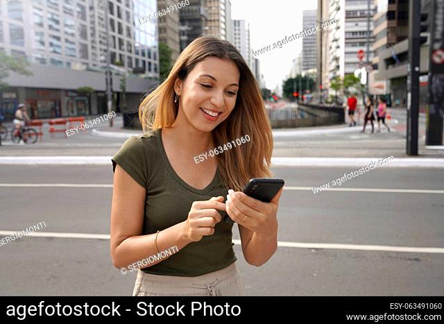Smiling girl using smartphone on Paulista Avenue, Sao Paulo, Brazil