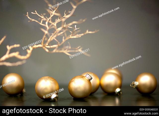 shiny and matt gold colored christmas tree toys and branch of a tree on a gray background