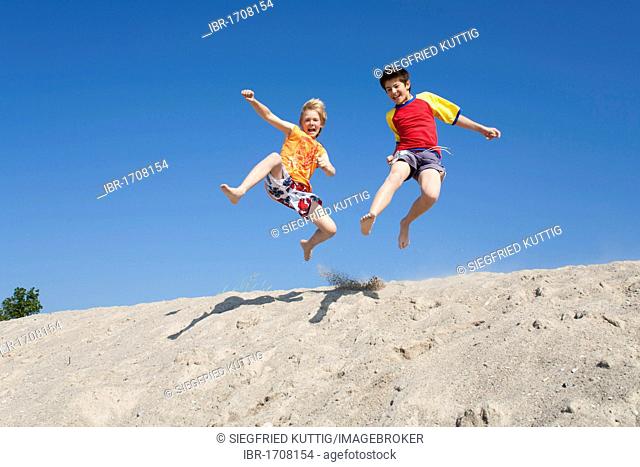 Two young boys laughing and jumping off a dune, Timmendorf, Poel island, Mecklenburg-Western Pomerania, Northern Germany