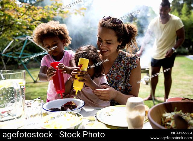 Mother and daughters enjoying barbecue lunch at backyard table