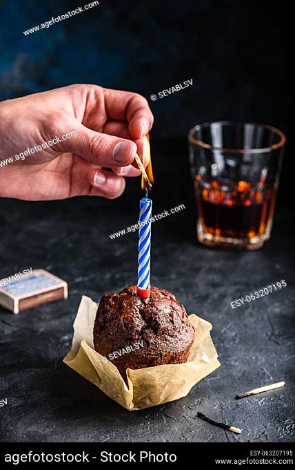 Hand lighting candle with a match on birthday chocolate muffin