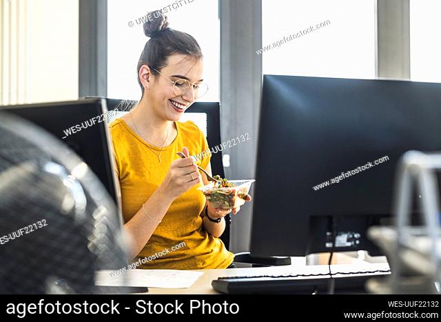 Smiling businesswoman eating food while sitting at office