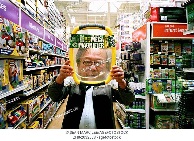 A elderly Asian man holds a giant magnifying toy over his face in a toy store in California