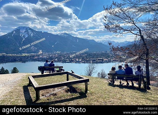 Hikers take a rest on the banks. Hikers on the Hoehenweg over the Tegernsee with a view of Rottach Egern on April 1st, 2021
