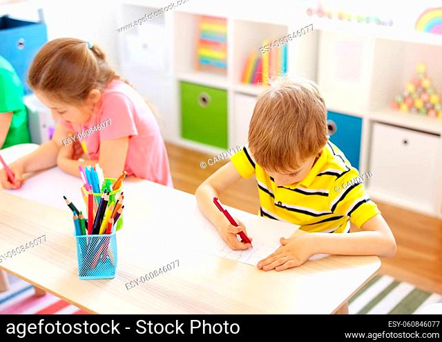 Schoolkids in the classroom sitting at the tables and writing a lesson. Concept of studying and learning at the school and kindergarten
