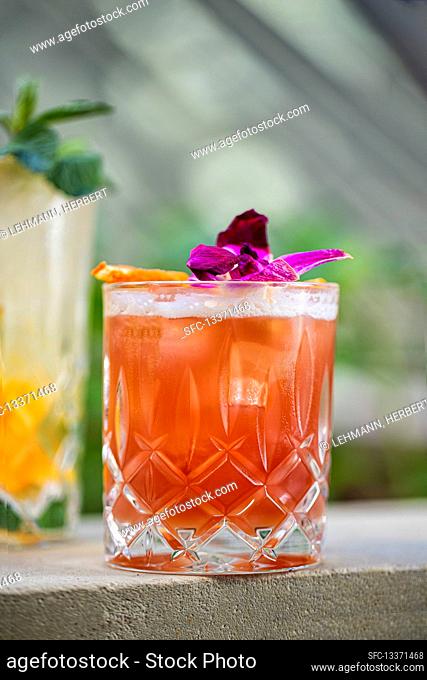 A pink cocktail in a glass decorated with an orchid flower