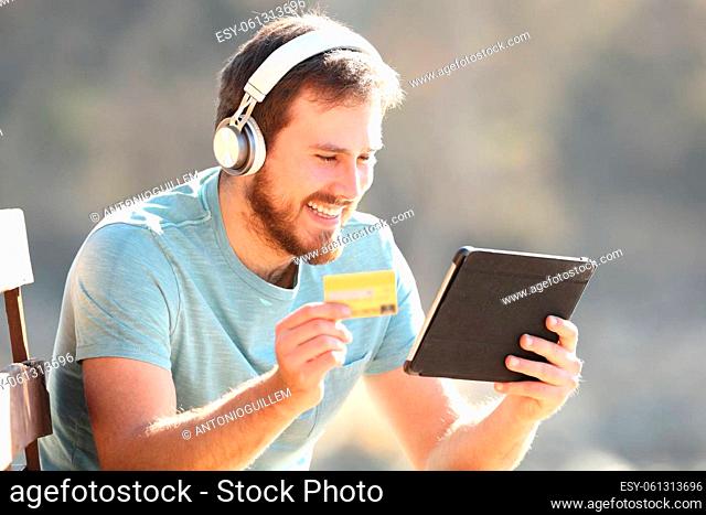 Happy man with headphones buying music or videos with a tablet and credit card online
