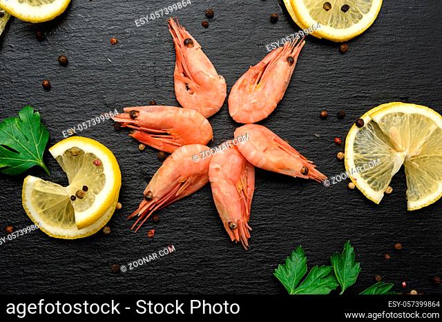 fresh shrimp and lemon slices on black board, top view