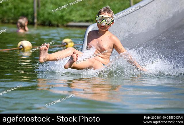 01 August 2020, Baden-Wuerttemberg, Uttenweiler: A boy slides down a water slide in a natural outdoor pool. Photo: Thomas Warnack/dpa