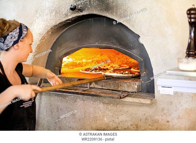 Female chef putting pizza in wood fired oven