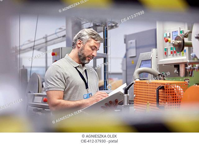 Male supervisor with clipboard at machinery control panel in fiber optics factory