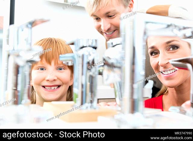 Low-angle portrait of a happy family, looking for a new bathroom sink faucet in a modern sanitary ware shop with high-quality fixtures and appliances