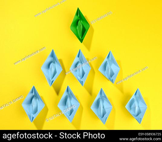 group of paper boats on a yellow background. concept of a strong leader in a team, manipulation of the masses, following new perspectives