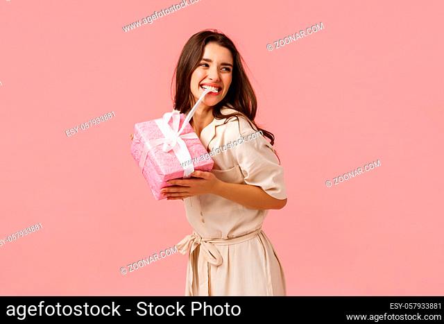 Happiness, tenderness and celebration concept. Carefree happy and upbeat young girl partying, having amazing birthday day, biting knot on cute gift, smiling