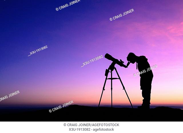 The silhouette of a teenage boy stargazing with a telescope at dusk