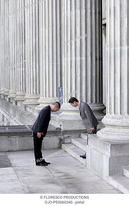 Two businessmen outdoors on steps bowing