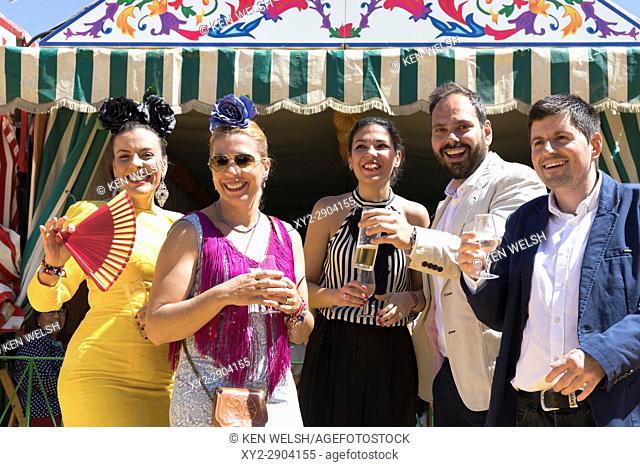 Seville, Seville Province, Andalusia, southern Spain. Feria de Abril, the April Fair. Group of happy friends raise their glasses