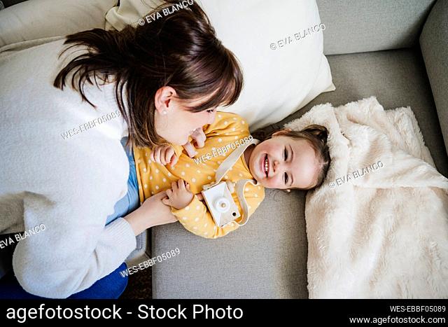 Playful mother tickling daughter on sofa