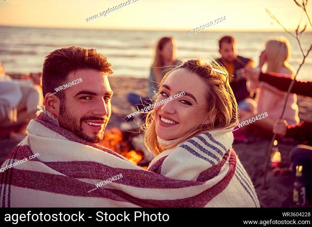 Young Couple enjoying with friends Around Campfire on The Beach At sunset drinking beer filter