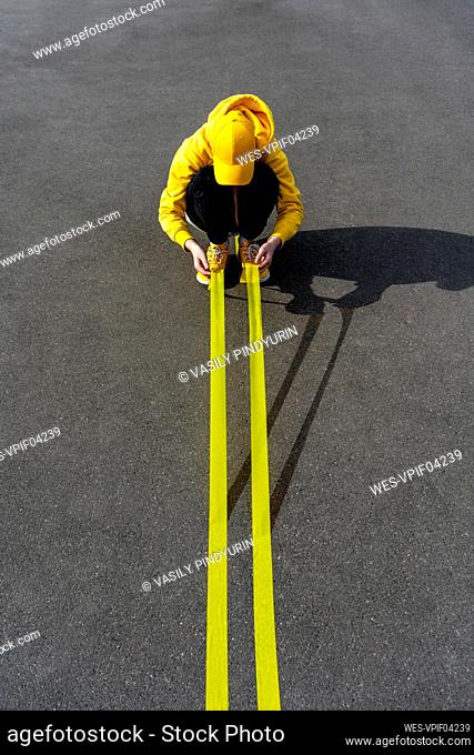 Boy holding yellow adhesive tapes while crouching on road