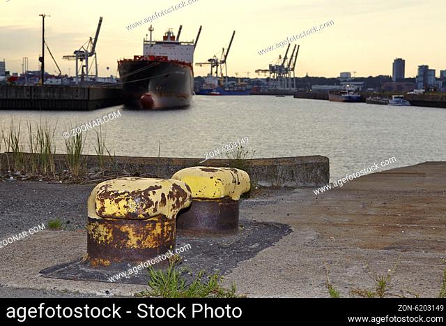 Alte Poller im Ellerholzhafen bei leichtem Gegenlicht vor einem Hafenbecken mit Containerschiff und Kränen fotografiert