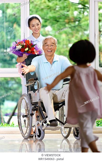Girl running towards to grandfather sitting in wheelchair