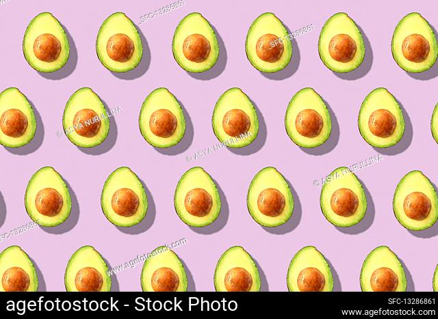 Lots of halved avocados in rows on a purple surface